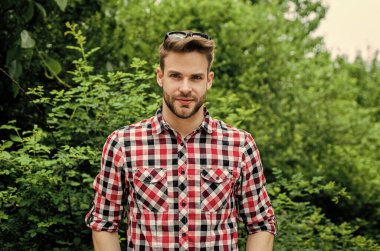 Harika bir tarzı var. Gündelik kıyafet. Gülümseyen adam kareli gömlek ve güneş gözlüğü takıyor. Yaz tatili konsepti. Açık havada kıllı yakışıklı bir adam. Erkek modası ve güzellik. Seksi sakallı maço