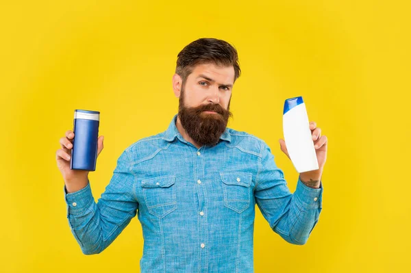 Brutale uomo barbuto scegliere bottiglia condizionatore di capelli su sfondo giallo, skincare — Foto Stock