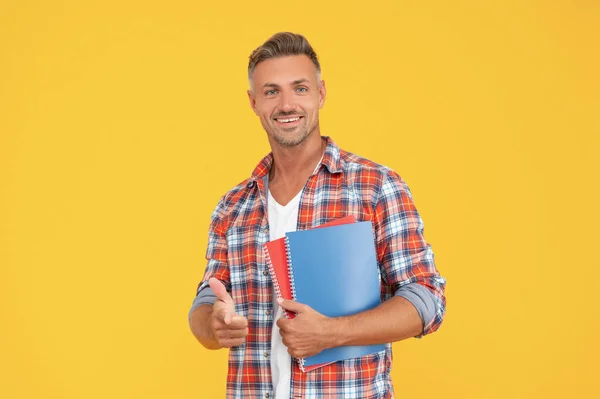 Homme heureux dans casual pointant doigt devant tenant livres scolaires fond jaune, étudiant — Photo