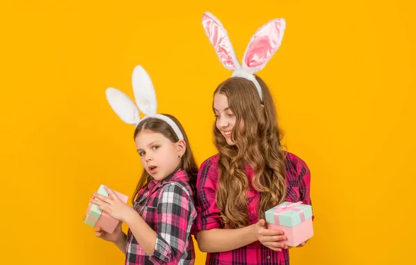 Положительные пасхальные дети в кроличьи уши держать подарочную коробку на желтом фоне — стоковое фото