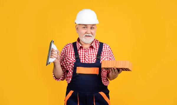 Fröhlicher älterer Herr Maurer mit Helm auf gelbem Hintergrund — Stockfoto