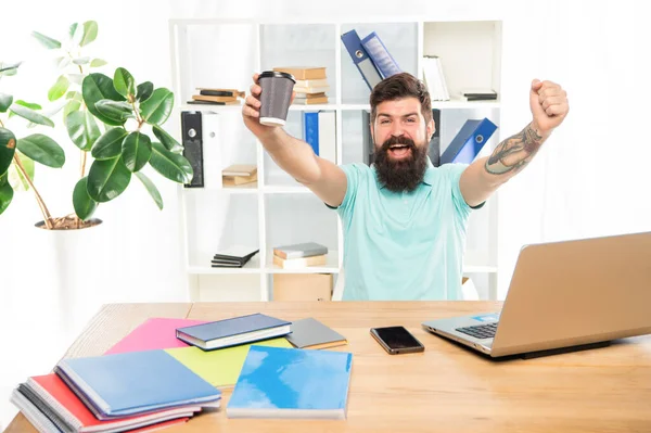 Hombre feliz sosteniendo una taza de café para llevar haciendo un gesto ganador en el escritorio de la oficina, romper —  Fotos de Stock