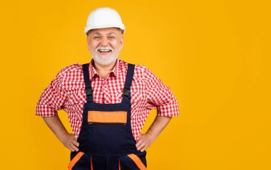 Sarı arka planda sert şapkalı neşeli kıdemli inşaatçı.