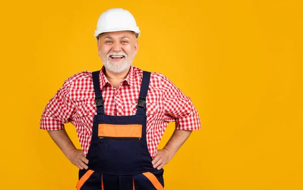Веселый старший мужчина строитель в каске на желтом фоне — стоковое фото