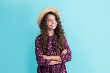 Hasır şapkalı mutlu çocuk, mavi arka planda uzun kahverengi kıvırcık saçlı.