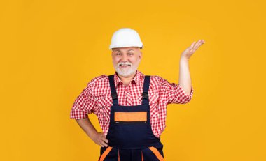 Sarı arka planda miğferli mutlu kıdemli inşaatçı.