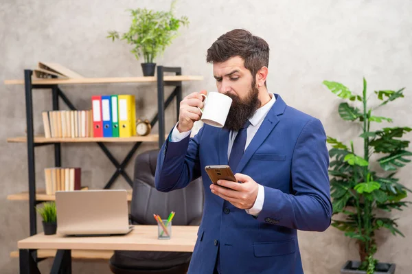 SMS para comunicación empresarial. Jefe leyendo el mensaje en el celular mientras bebe café. Mensajería SMS —  Fotos de Stock