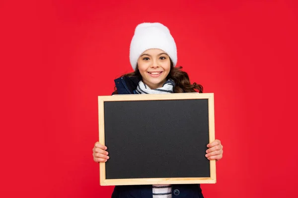 Vendas de inverno. Miúdo positivo com quadro-negro de chapéu. menina adolescente segurando quadro com espaço de cópia. — Fotografia de Stock
