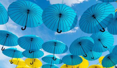 Gökyüzünde asılı mavi ve sarı şemsiyeler. Şemsiye geçmişi. Sokak dekorasyonu