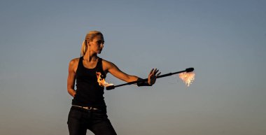 Ateşli seksi kadın ateş sanatçısı yanan batonu manipüle ediyor. Açık havada mavi gökyüzü dönüyor.