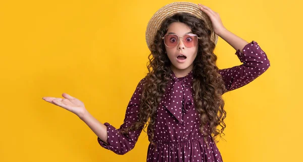 Niño sorprendido en sombrero de paja y gafas de sol con pelo rizado largo morena presentando producto — Foto de Stock