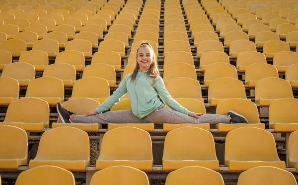 Chica feliz gimnasta hacer splits estirar las piernas en los asientos del estadio, gimnasia —  Fotos de Stock