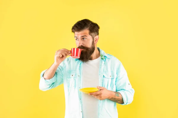 Серьезный кавказский мужчина пьет кофе из чашки держа блюдце желтый фон, кофеин — стоковое фото