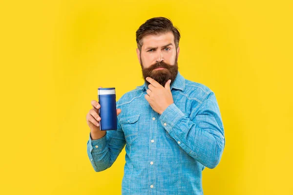 Жорстокий чоловік тримає пляшку шампуню на жовтому тлі, догляд за волоссям. торкатися бороди — стокове фото