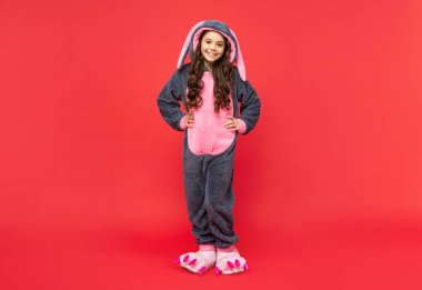 Kırmızı arka planda rahat ve rahat bir uyku elbisesi içinde mutlu bir çocuk.