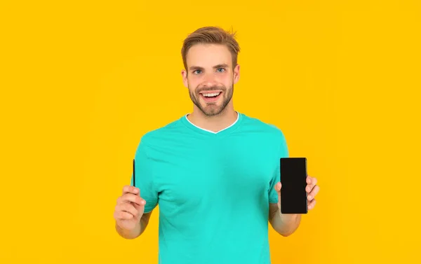 노란색 배경에 스마트폰을 보여 주는 행복 한 남자. 제품 제안. — 스톡 사진