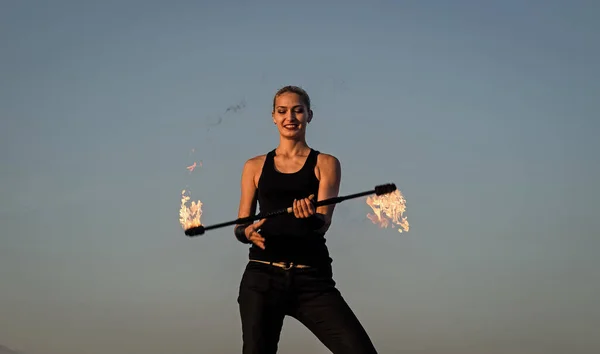 Happy sexy fire performer woman manipulate flaming baton on blue sky outdoors, performance