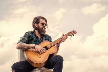 Müziğe benziyor. Uzun saçlı hippi ve bıyıklı gitarist. Müzik aleti olan erkek gitarist. Country müzik konsepti. Sakallı adam akustik gitar çalar. Sıradan bir adam insani duygularını ifade eder.