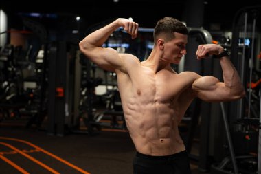 Kaslı gövdeli güçlü bir adam. Kol kasları kaslı. Spor salonunda çift kol kasları var.