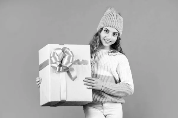 От Санты. Рождество наступило. зимний праздник сюрприз. маленькая девочка вязала шляпу и свитер. Ребенок держит в руках коробку оранжевого цвета. С новым 2020 годом. Служба доставки подарков. торговые преимущества — стоковое фото