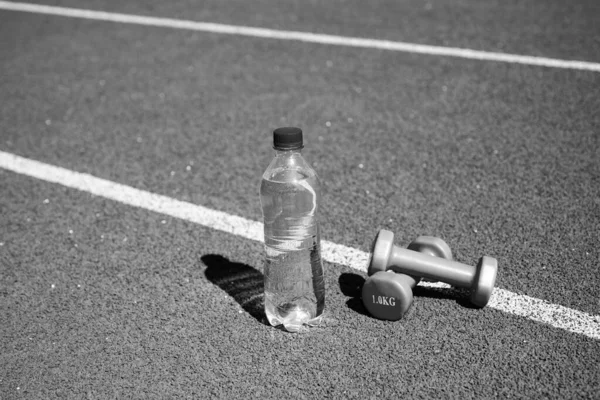 Butelka wody i sztangi fitness na torze stadionu, zdrowie — Zdjęcie stockowe