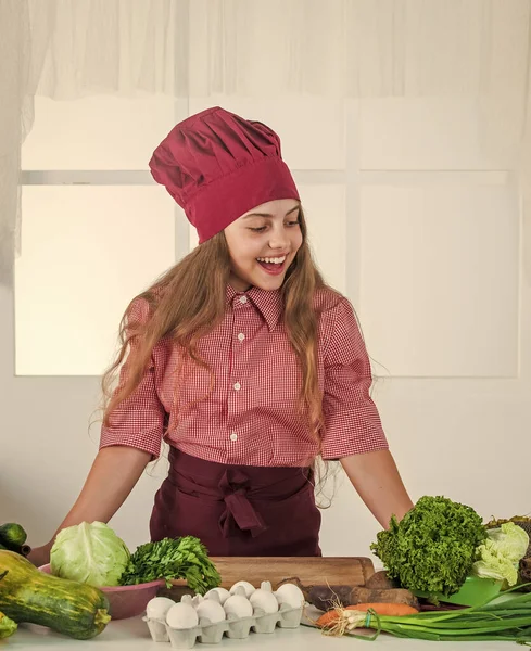 Feliz chica adolescente cocinar verduras. niño vistiendo uniforme de chef profesional. — Foto de Stock