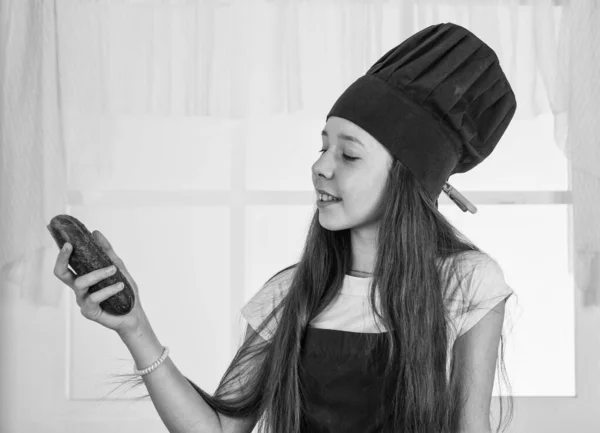 Pensa verde. Menina chef em chapéu e avental. miúdo a cozinhar comida na cozinha. escolher uma carreira. ajudante com pepino. culinária e culinária. infância feliz. criança feliz desgaste cozinhar uniforme — Fotografia de Stock