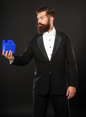 Smokinli bir adam siyah arka planda resmi kravat takıyor ve erkekler günü için bir kutu hazırlıyor.
