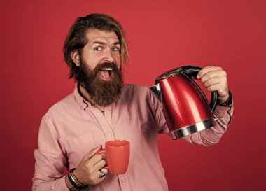 Çay içme zamanı konsepti. Gömlekli sakallı adam elektrikli su ısıtıcısı tutuyor. Sıradan bir adam modern teknolojiyi günlük hayatta kullanır. Bıyıklı mutlu hipster, kaynar su. erkek evi.