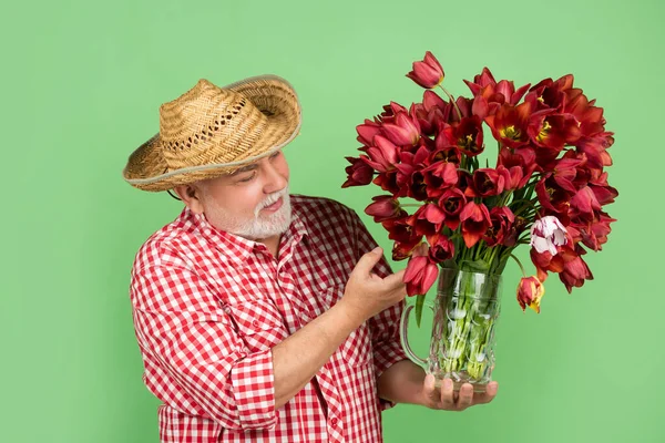 头戴礼帽、开朗的老人拿着绿色背景的春天郁金香花 — 图库照片
