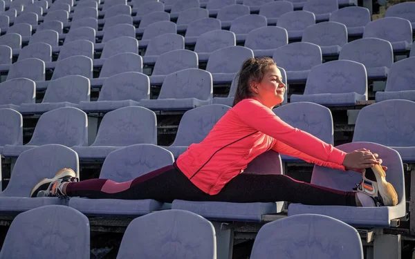 Flexibel meisje kind in sportkleding doen splitst stretching benen op stadionstoelen, flexibiliteit — Stockfoto