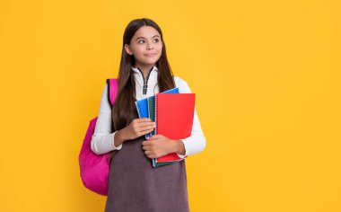 Okul çantası ve sarı arka planda el kitabı olan mutlu çocuk.