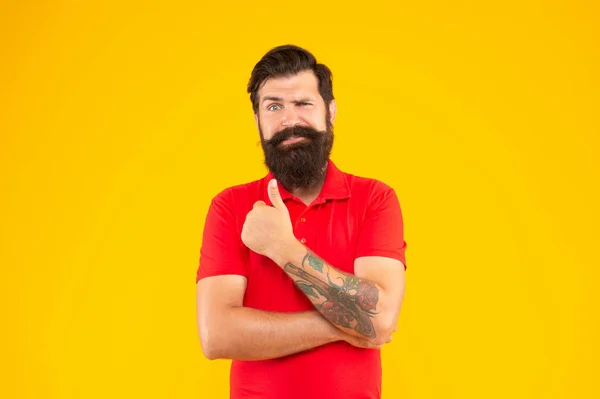 Confuso ragazzo con barba e acconciatura mostrando pollice su sfondo giallo, mens bellezza — Foto Stock