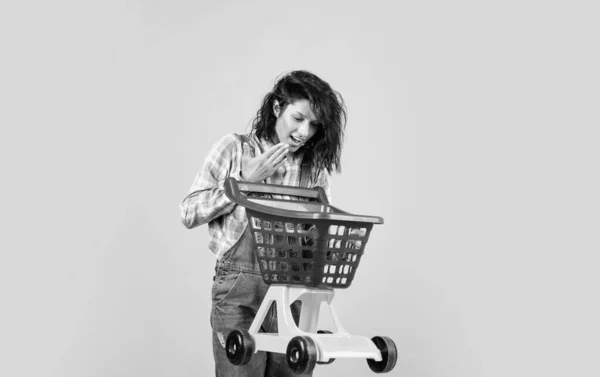 Wesoła dama w stylu dżinsowym nosić wózek na żółtym tle, zakupy — Zdjęcie stockowe