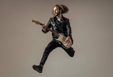 duygusal sakallı rock müzisyeni elektro gitar çalıyor deri ceketle ve zıplayarak, gitarist