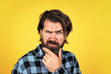 Fotoğraf için poz vermek. Bıyıklı, olgun bir adam. İnsan duygularını ifade etmek. Kareli gömlekli ciddi bir adam. Sarı arka plandaki duygusal adam. Vahşi sakallı hippi.
