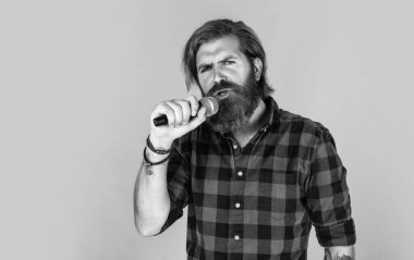Mikrofonda şarkı söyleyen sakallı adam. Sahnede özgüven ve karizma. Kareli gömlek giyen sakallı bir adam. Rock müzik. Erkek karaoke şarkıcısı. Olgun karizmatik erkek vokalist. Boşluğu kopyala
