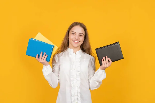 Улыбающаяся девочка держит школьную тетрадь на желтом фоне, учится — стоковое фото
