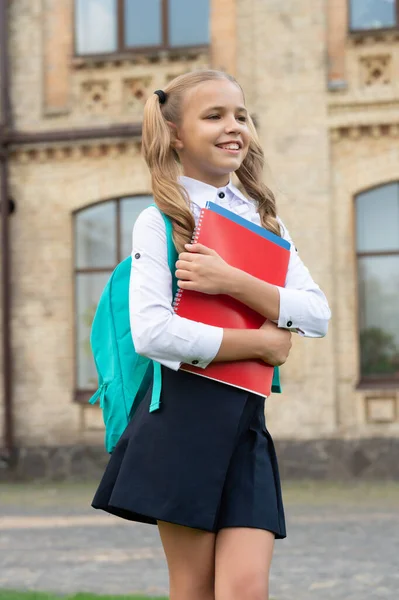 Szczęśliwy dzieciak w mundurze z powrotem do szkoły niosąc książki i plecak, edukacja — Zdjęcie stockowe