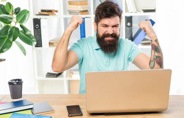 兴奋的男人在办公室的笔记本电脑上做着获胜的手势，事业有成 — 图库照片