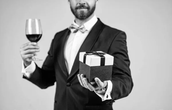 Elegante man met ongeschoren gezicht bijgesneden uitzicht in vakantie feestelijke kleding houden rode wijn glas en geschenkdoos grijze achtergrond, feest — Stockfoto