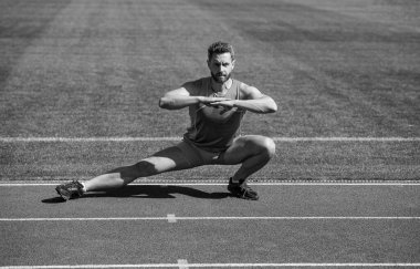 Atletik koşucu esneme egzersizi yapıyor. Sabah antrenmanına hazırlanıyor, ısınıyor.