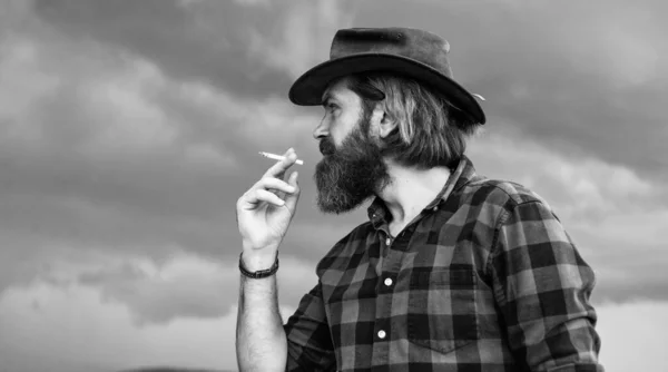 Modo de vida pouco saudável. conceito de fumar. maduro brutal hipster em chapéu de cowboy e camisa quadriculada. estilo de moda casual. Homem barbudo segurando cigarro. maus hábitos prejudiciais — Fotografia de Stock