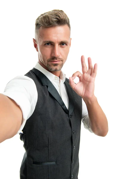Hombre de negocios serio en chaleco de traje tomando selfie mostrando OK anillo gesto aislado en blanco, bien — Foto de Stock