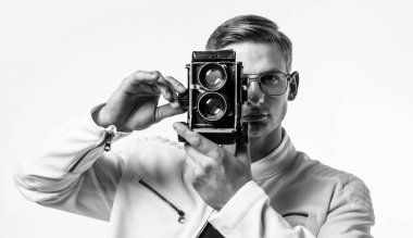 Bu kamera parmaklarınızın ucunda bir olasılıklar dünyası oluşturur. Genç fotoğrafçı beyazda izole edilmiş. Yakışıklı adam klasik fotoğraf makinesiyle fotoğraf çekiyor. Fotoğraf ekipmanları. Çekim oturumu