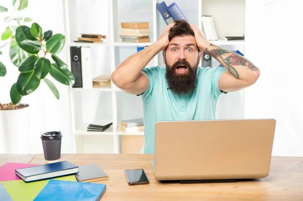 Překvapený muž s čelistí svěšenou svírající hlavu sedí u laptopu v kanceláři, překvapení — Stock fotografie