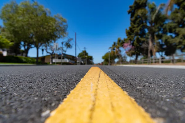 Желтая линия дороги с разметкой на поверхности асфальтированной дороги вдоль размытой жилой улицы в пригороде — стоковое фото