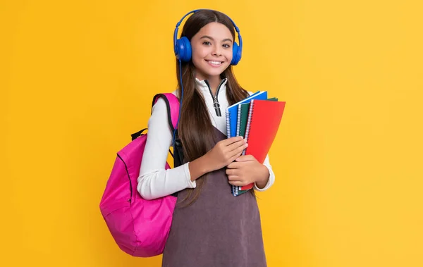 Positivt barn i hörlurar med skola ryggsäck med arbetsbok på gul bakgrund — Stockfoto