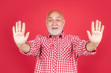 Kırmızı arka planda kareli gömlekli, olgun bir adam şaşırdı.