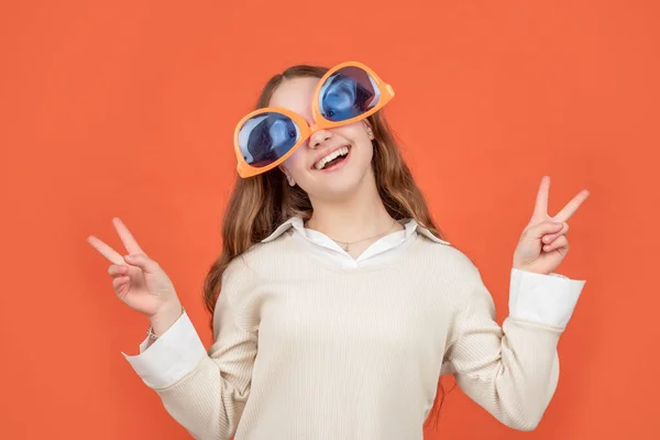 Gelukkig meisje dragen groot grappig zonnebril ondersteboven maken V-zingt gebaar bruin achtergrond, overwinning — Stockfoto